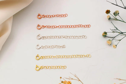 Set of gold necklaces on a light surface with dried flowers.