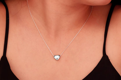 A close-up image of a person wearing a dainty silver necklace with a 3D moveable heart pendant in gold color.