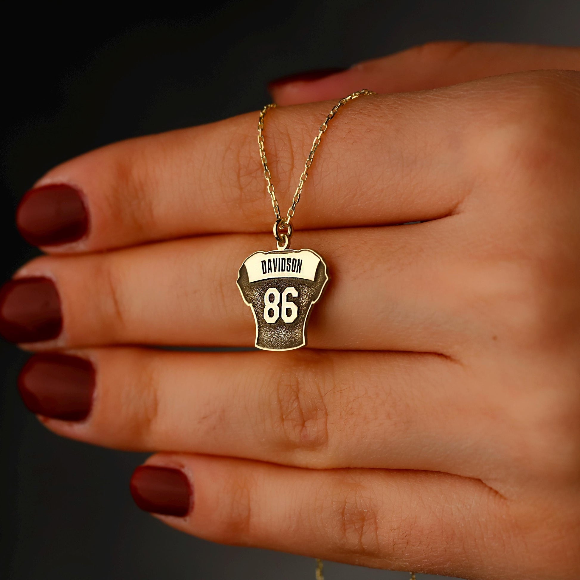 Hand holding a gold necklace with a pendant featuring the number 86 and 'DAVIDSON' text.
