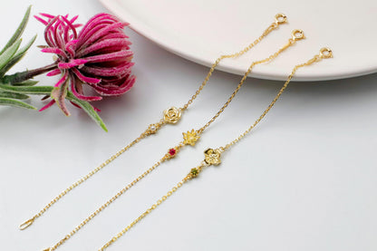 Two gold flower design necklaces with decorative elements on a white surface with a pink flower.