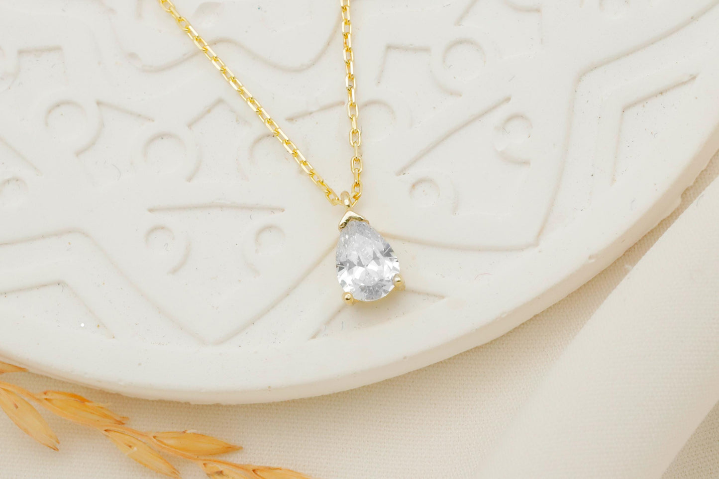 Gold necklace with a teardrop-shaped clear gemstone on a textured white surface