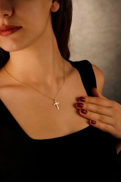 Woman wearing a gold necklace with a cross pendant against a neutral background