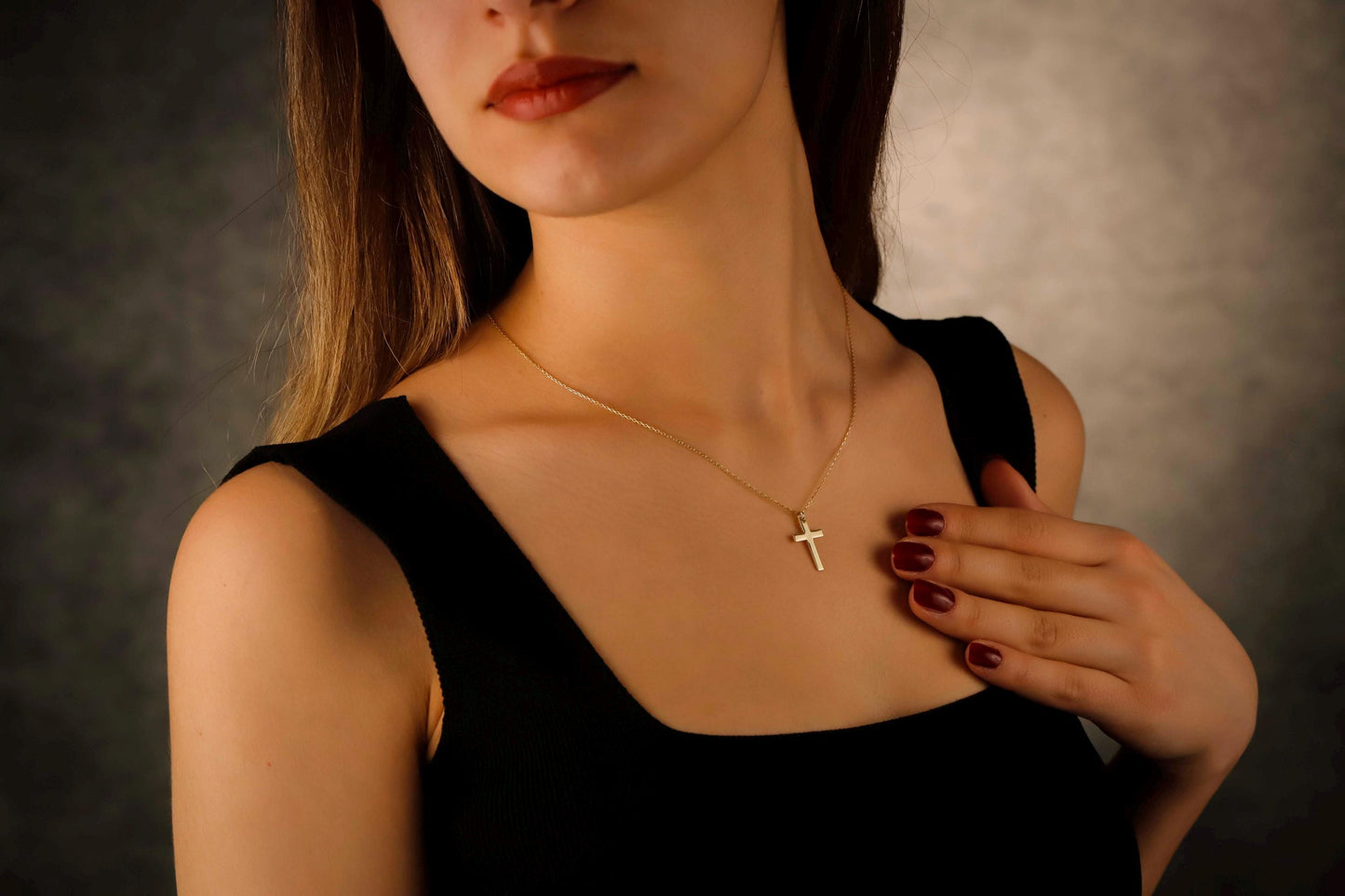 Woman wearing a gold necklace with a cross pendant against a neutral background