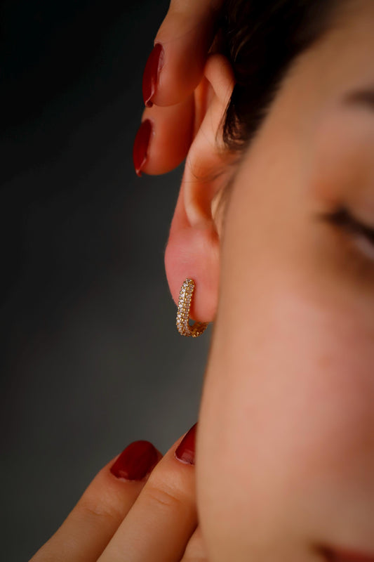 Close-up of a person wearing a gold hoop earring with a blurred background
