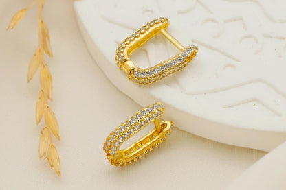 Gold hoop earrings with embedded stones on a textured beige surface.