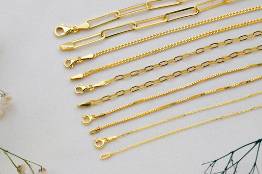 Gold chains of various designs on a light gray background