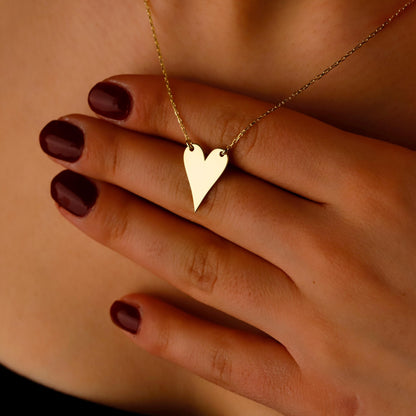 Gold heart-shaped necklace worn by a person with dark nail polish.