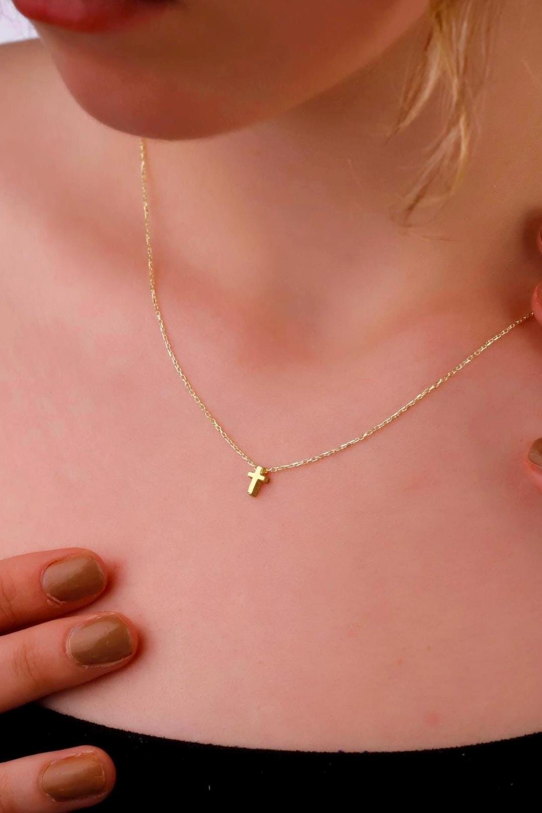 Gold necklace with a small cross pendant on a person's neck