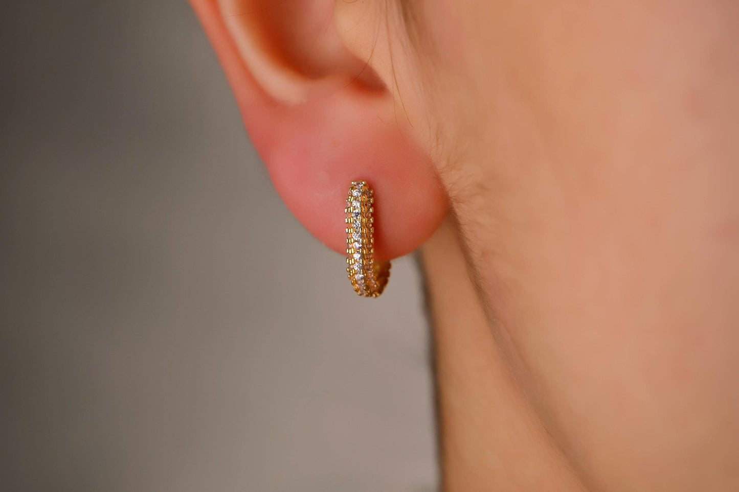Close-up of a person wearing a gold hoop earring with a blurred background