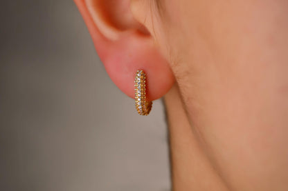 Close-up of a person wearing a gold hoop earring with a blurred background