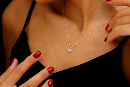 A close-up image of a woman wearing a 14K gold pave diamond heart necklace with a silver chain, showcased on a black dress.
