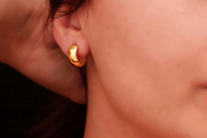 A close-up image of a woman's ear wearing a gold-colored chunky hoop earring.