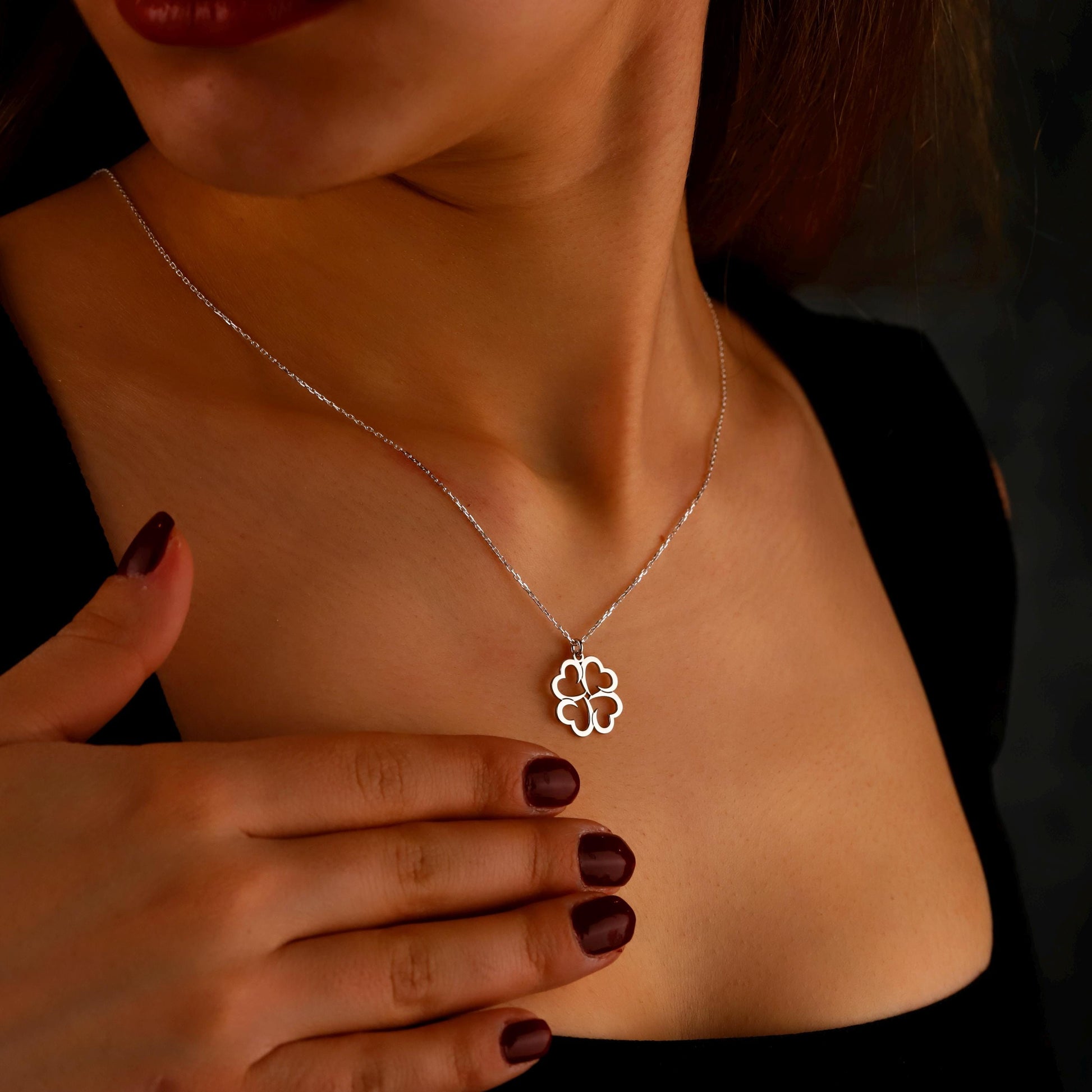 Silver necklace with a clover pendant worn by a person against a dark background