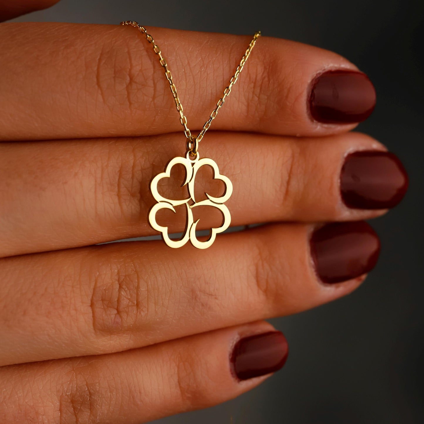 Gold four-leaf clover necklace on a hand with dark nail polish against a dark background