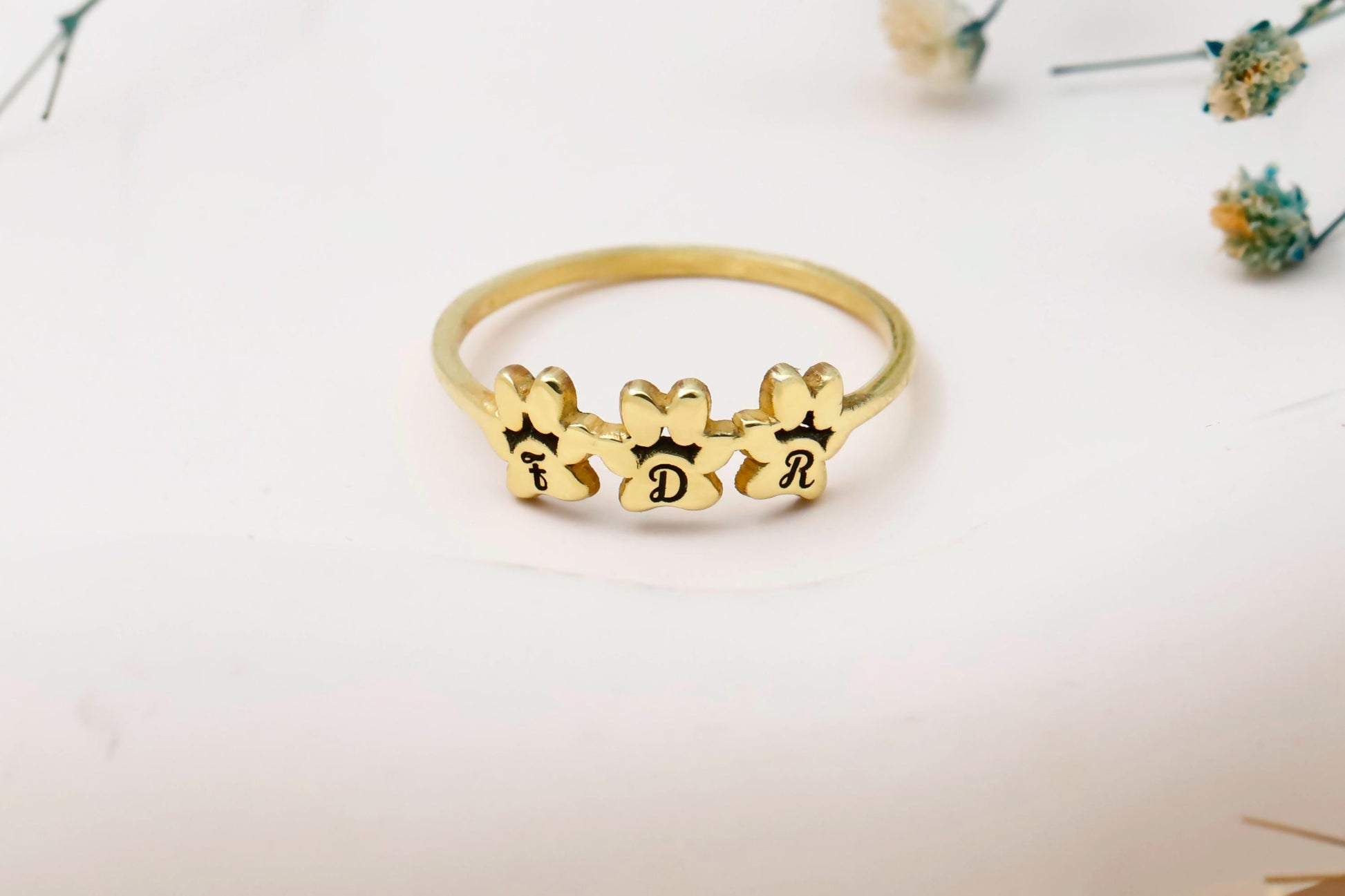 Gold ring with bear-shaped charms and initials on a light background
