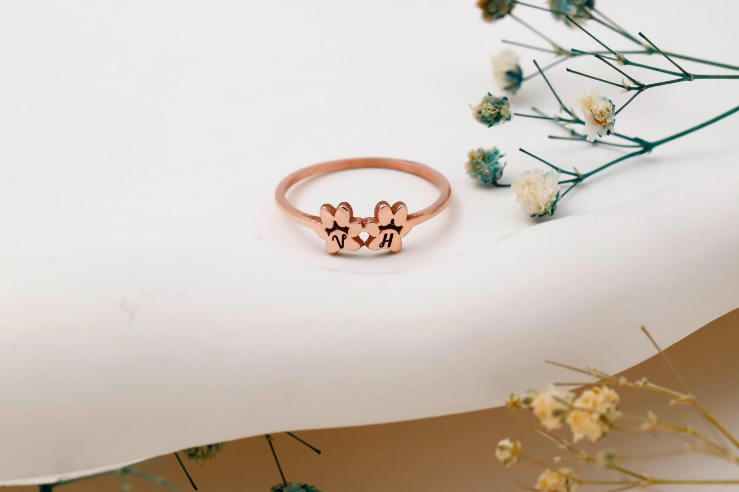 Rose gold ring with paw prints on a white surface with dried flowers.