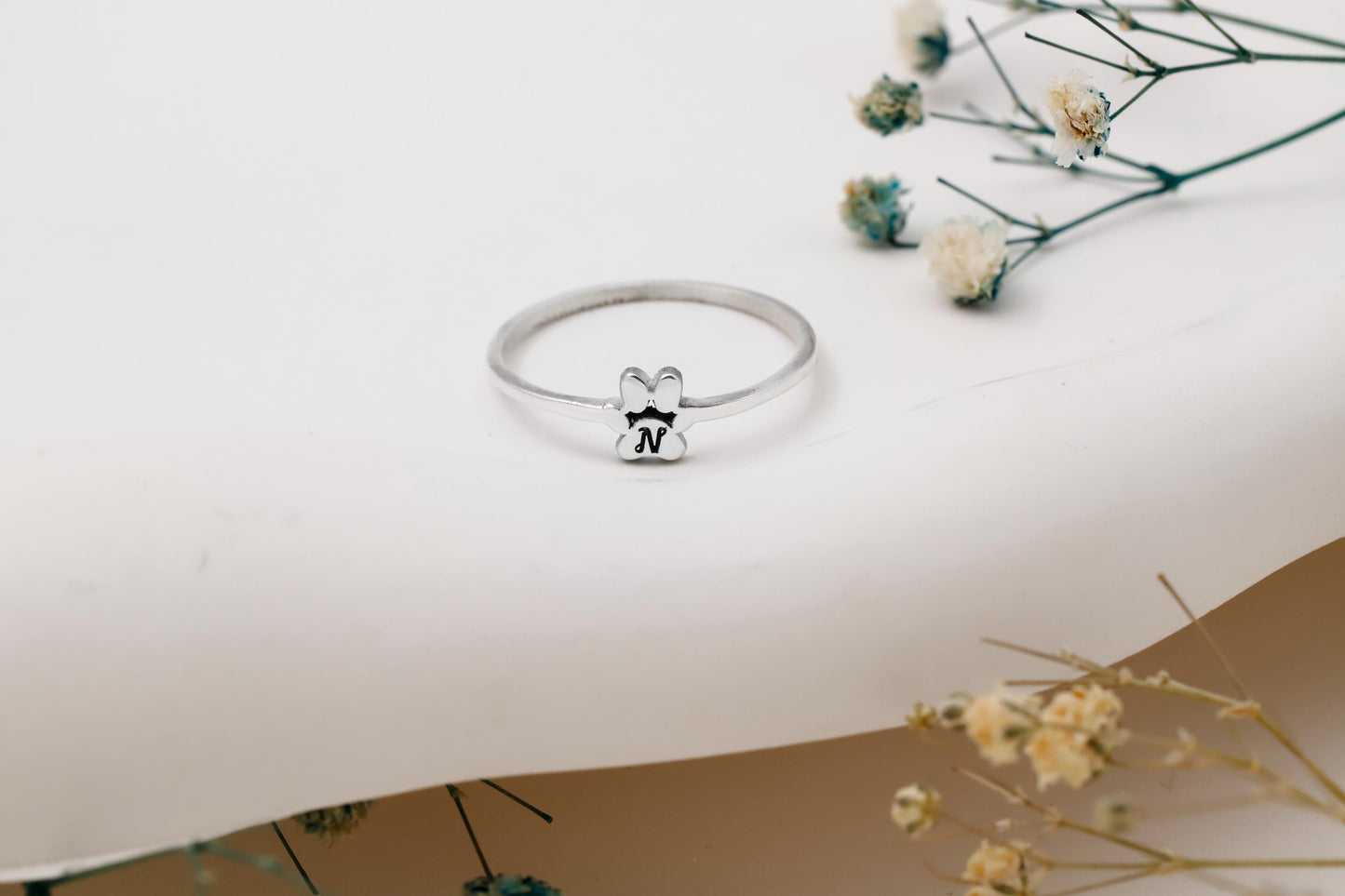 Silver ring with a small bear charm on a white surface with dried flowers.