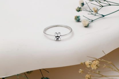Silver ring with a small bear charm on a white surface with dried flowers.