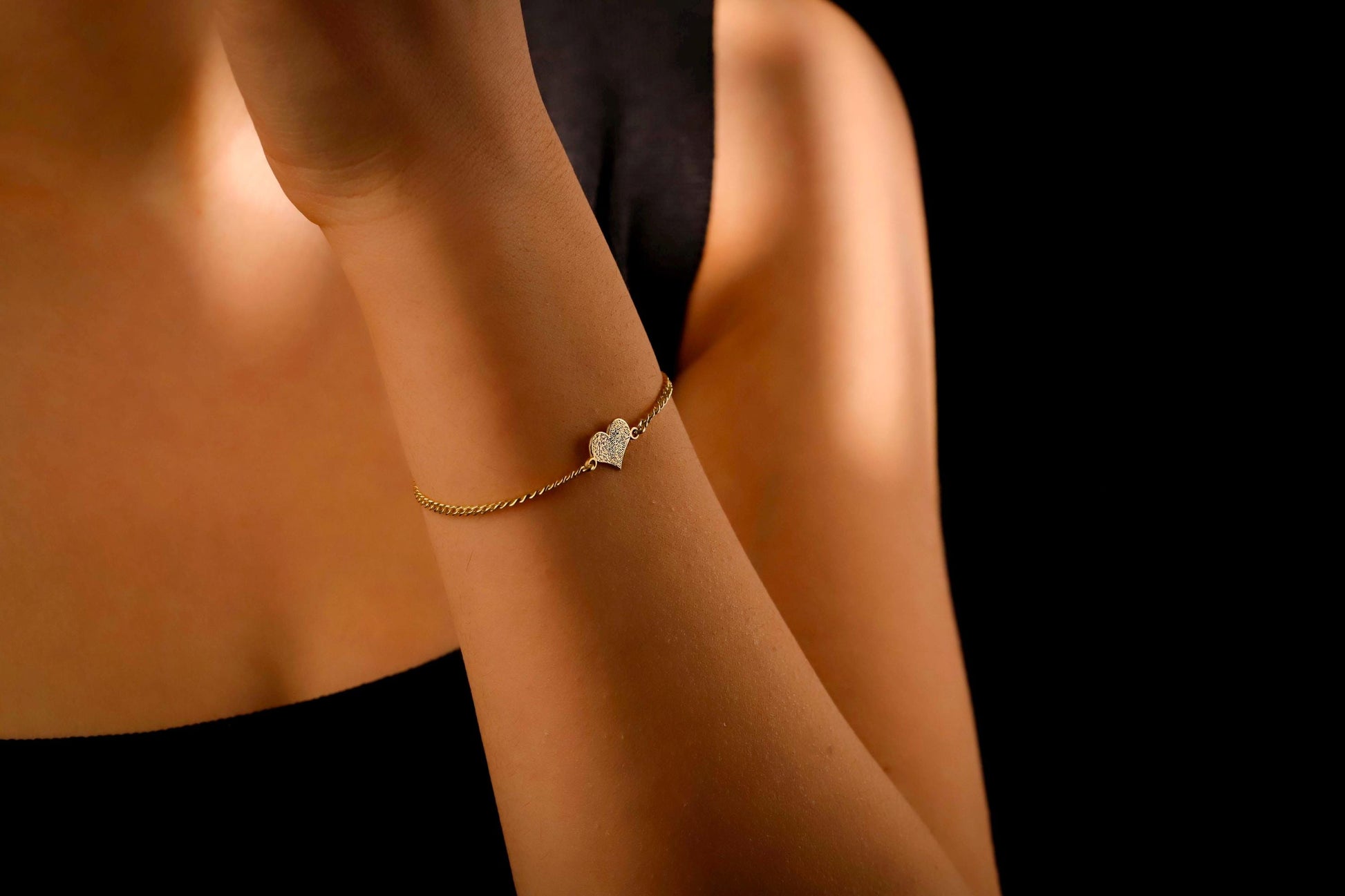Gold bracelet with a heart charm on a person's wrist against a black background
