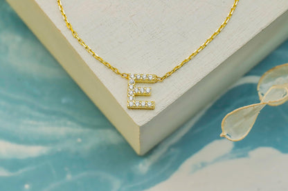 Gold necklace with a letter 'E' pendant on a light blue surface