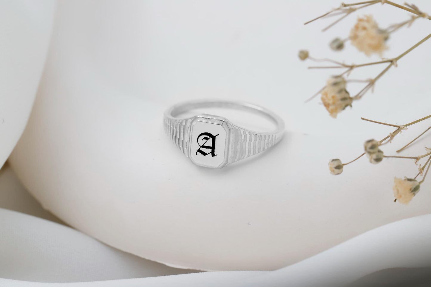 Silver ring with an 'A' on a white surface with dried flowers