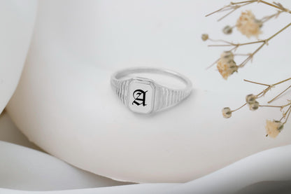Silver ring with an 'A' on a white surface with dried flowers