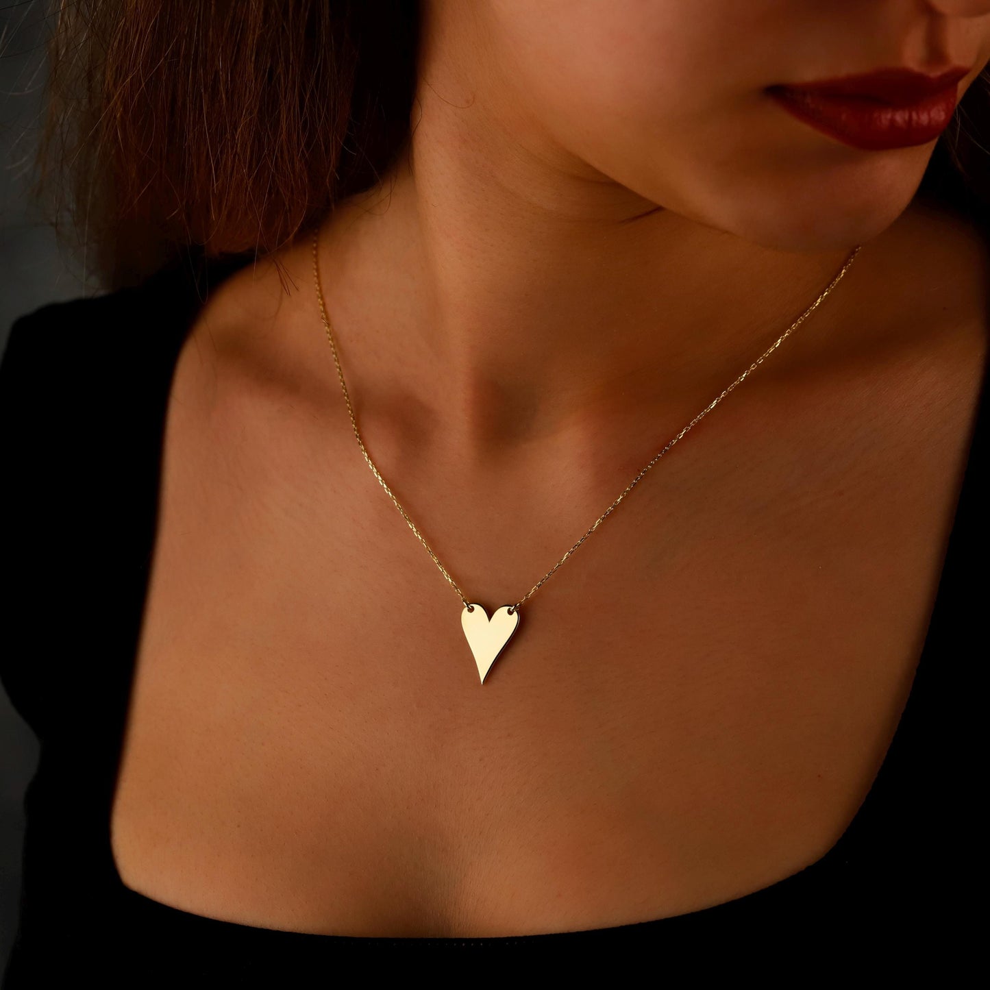Gold heart necklace on a person with a dark background