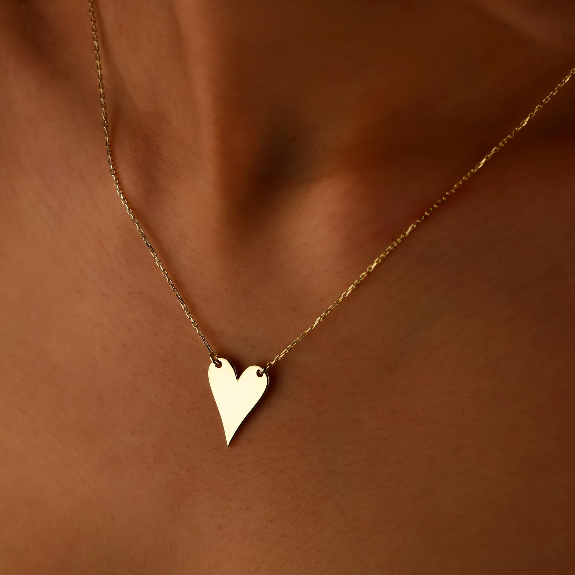 Gold heart-shaped necklace on a person's neck against a brown background