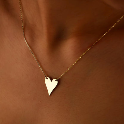 Gold heart-shaped necklace on a person's neck against a brown background