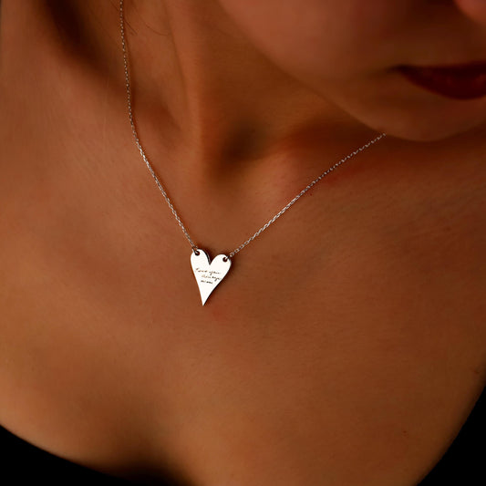 Silver heart-shaped necklace on a person's neck with a warm background