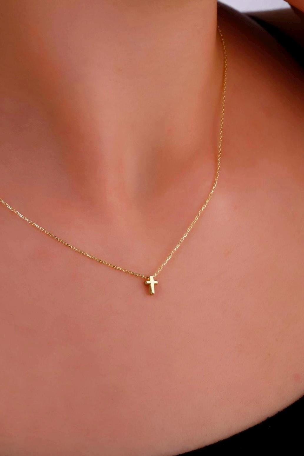 Gold necklace with a small cross pendant on a person's neck