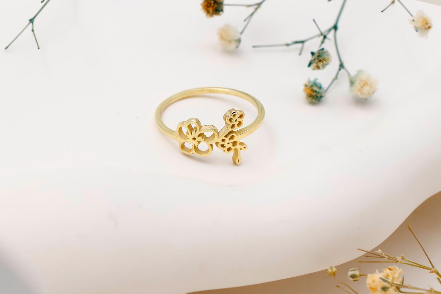 Gold ring with floral design on a white surface with dried flowers.