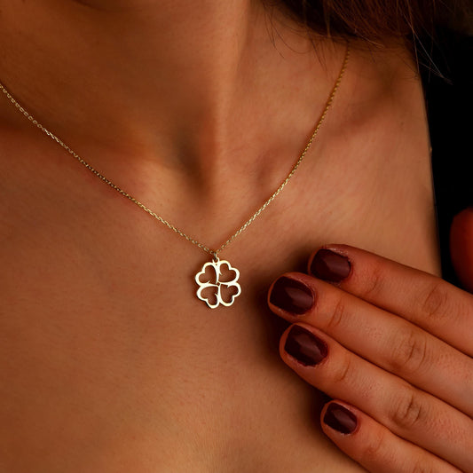 Gold necklace with a clover pendant worn by a person with dark nail polish.