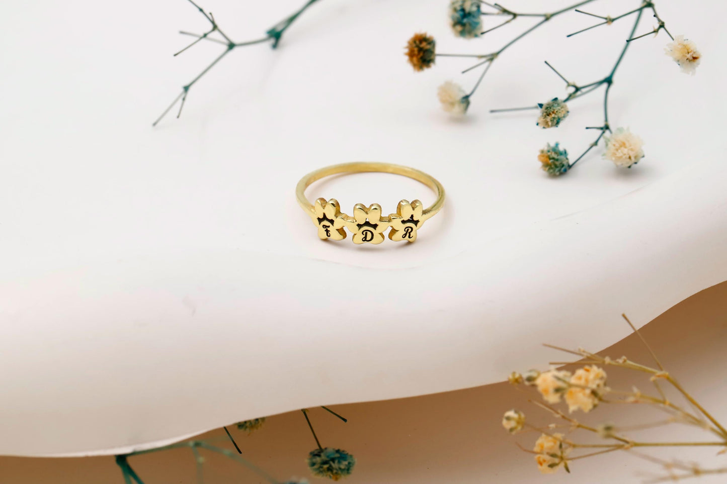 Gold ring with floral design on a white surface with dried flowers