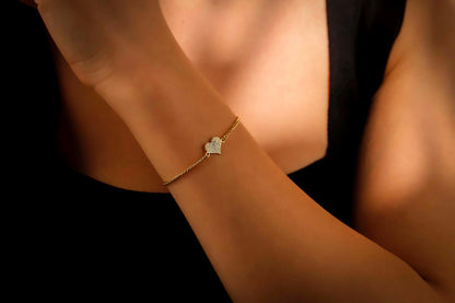 Gold bracelet with a heart charm on a wrist against a dark background