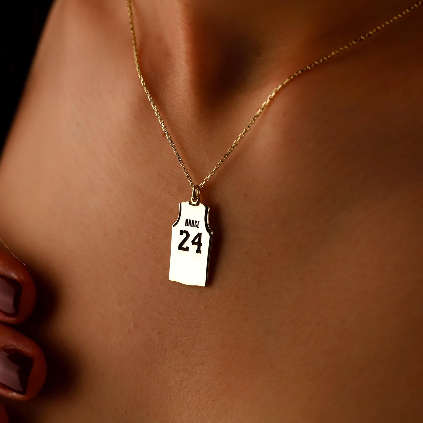 Necklace with a pendant shaped like a basketball jersey number 24 on a person's neck.
