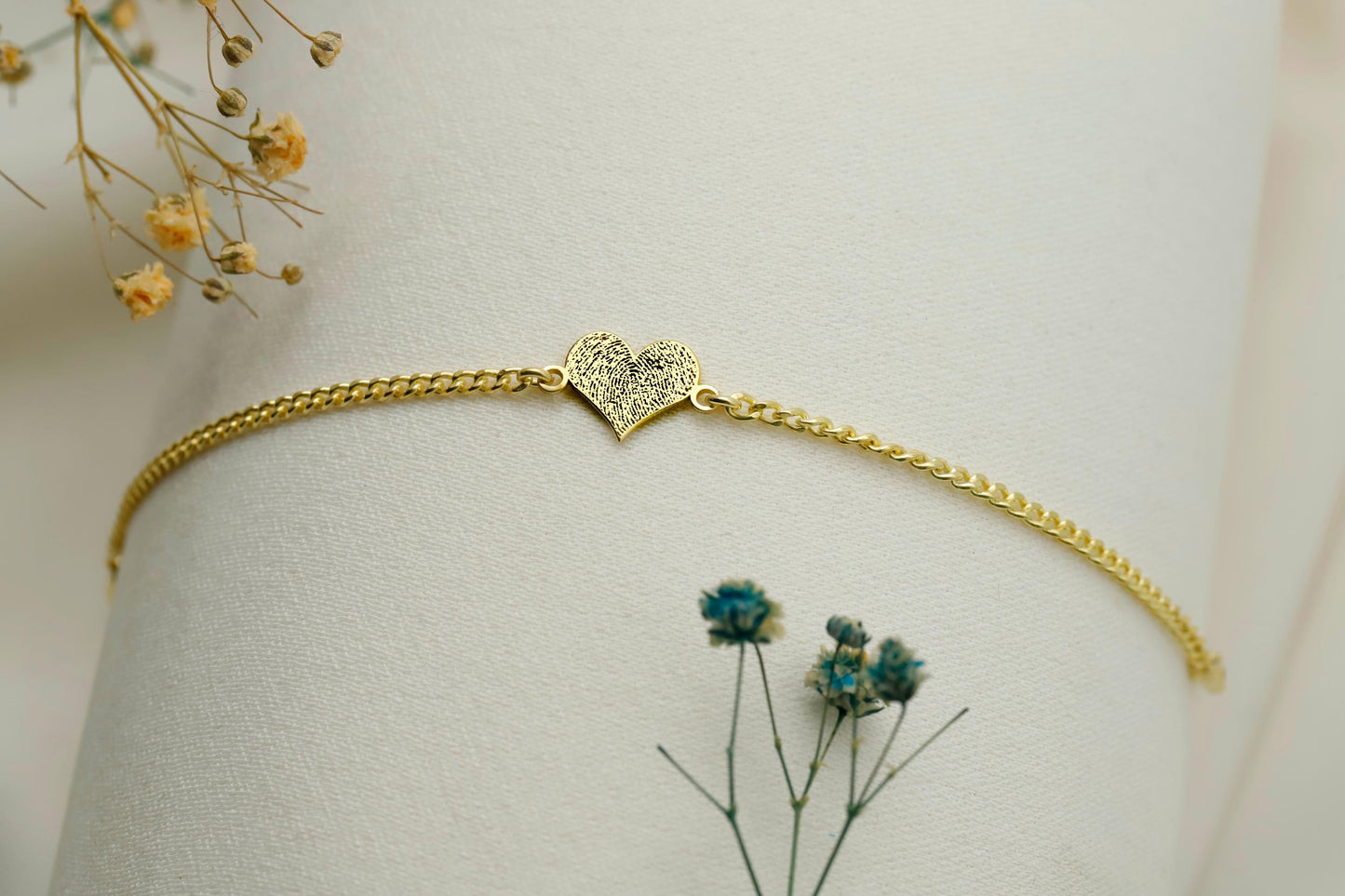 Gold bracelet with a heart-shaped clasp on a light background with dried flowers.
