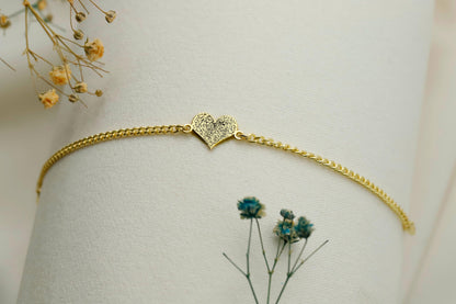 Gold bracelet with a heart-shaped clasp on a light background with dried flowers.