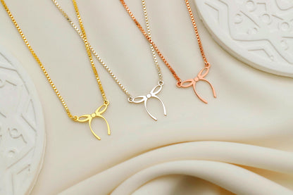 Three gold, silver, and rose gold necklaces with bow pendants on a textured beige surface.