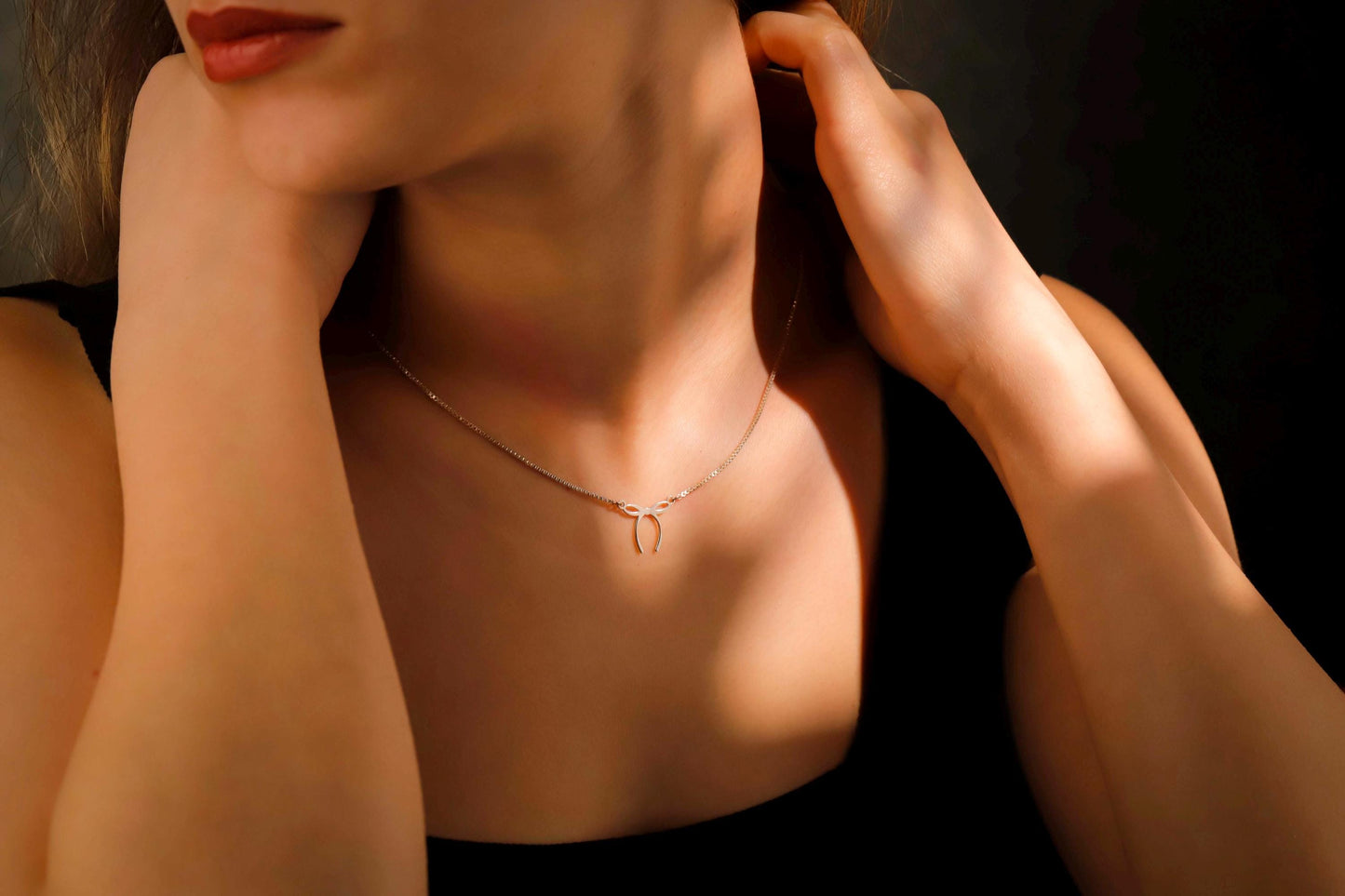 Close-up of a person wearing a delicate necklace with a dark background