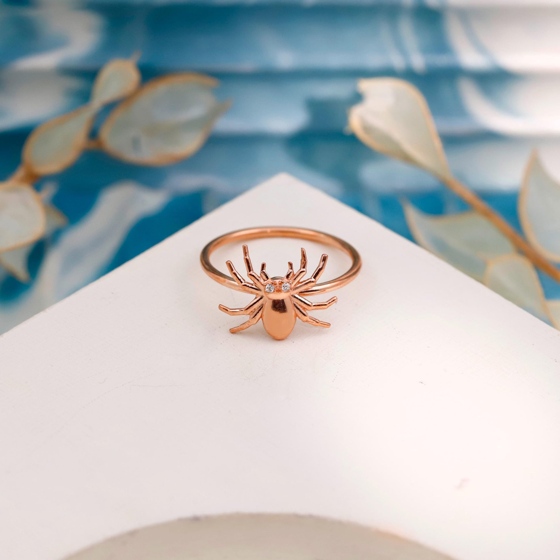 Rose gold spider ring on a white stand with a floral background
