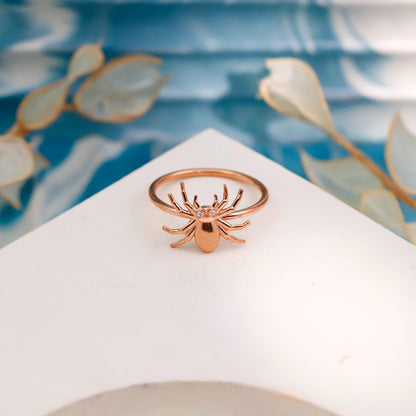 Rose gold spider ring on a white stand with a floral background