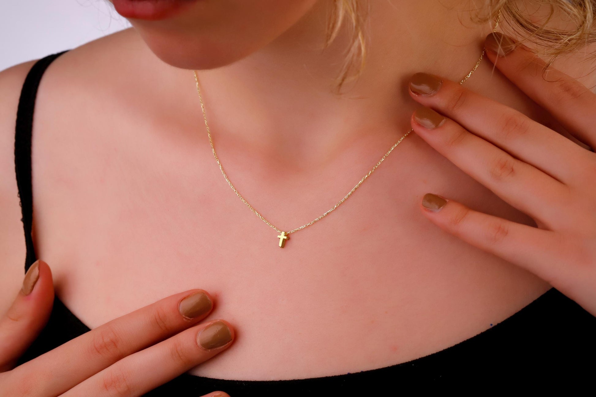 Gold necklace with a small cross pendant on a person's neck