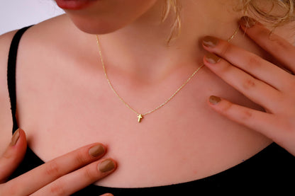 Gold necklace with a small cross pendant on a person's neck
