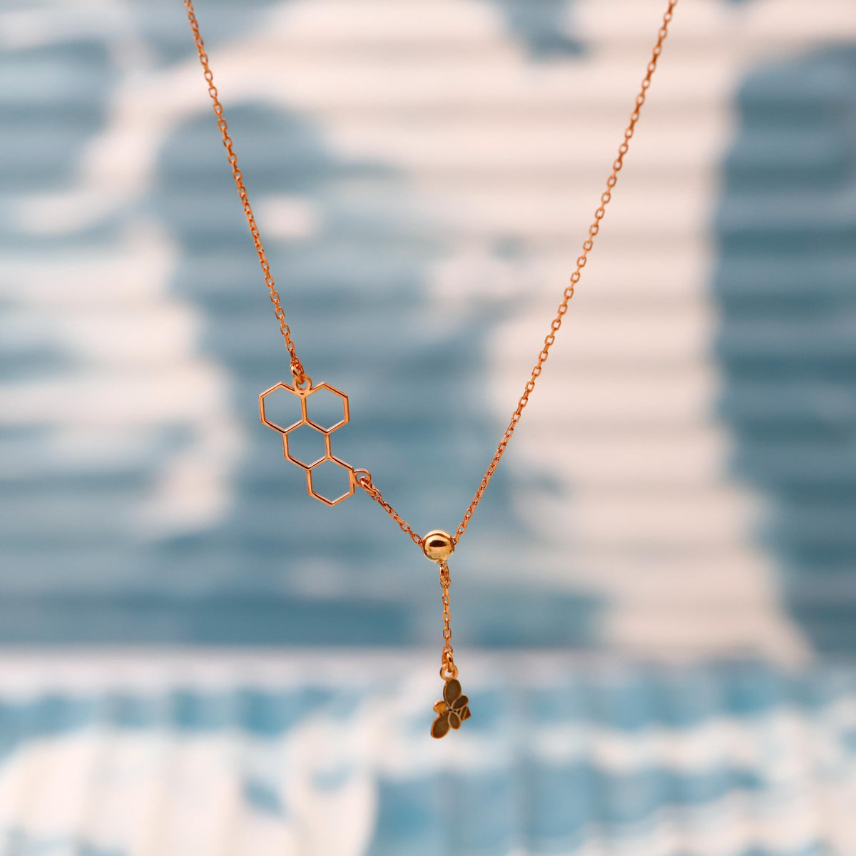 Gold necklace with honeycomb and clover pendant on a blurred blue and white background