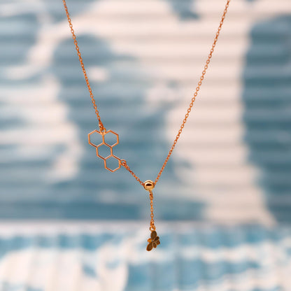 Gold necklace with honeycomb and clover pendant on a blurred blue and white background