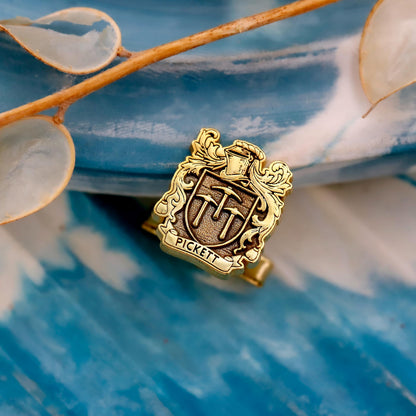 Gold crest-shaped cufflinks with 'Pickett' engraved on a blue and white floral background