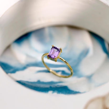 Gold ring with a purple gemstone on a white and blue patterned surface