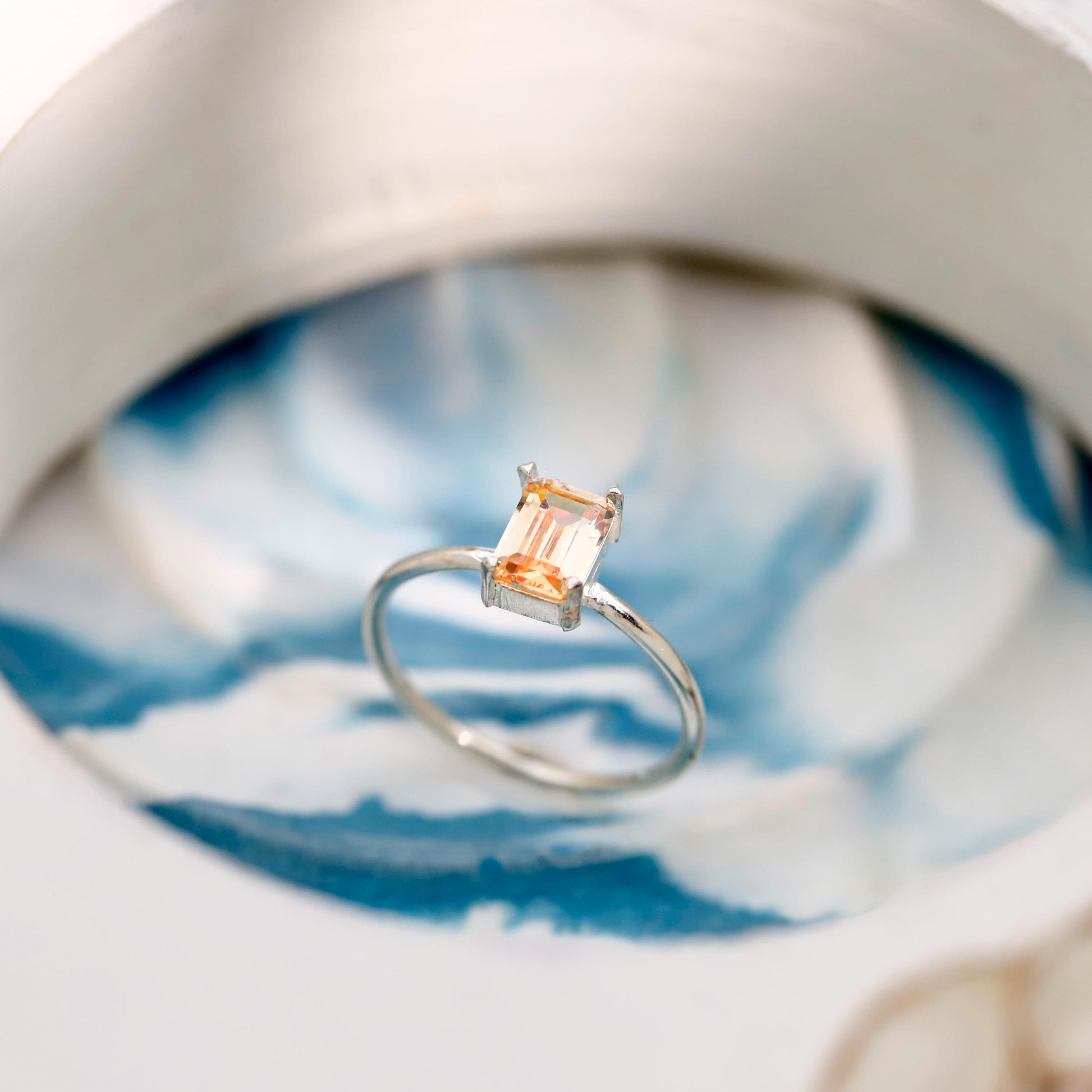 Silver ring with a rectangular gemstone on a blue and white ceramic dish