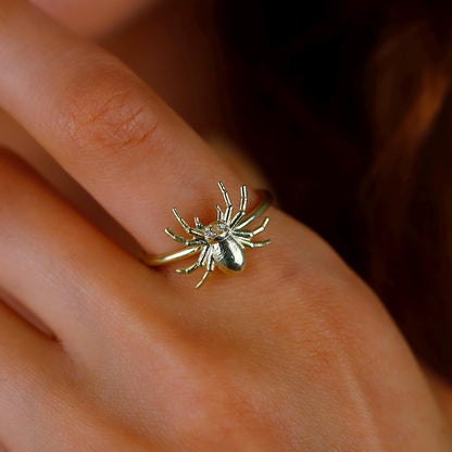 Gold spider-shaped ring on a person's finger with a blurred background
